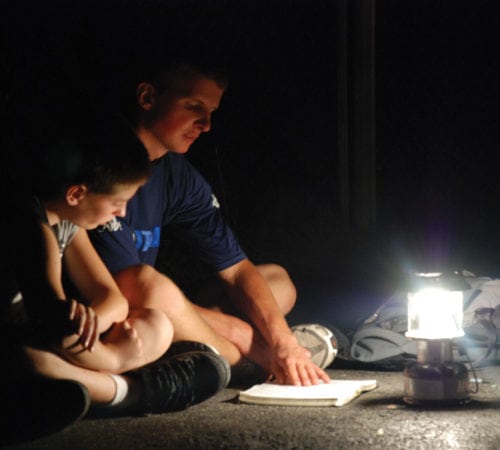 A camper and a leader reading by lantern light.