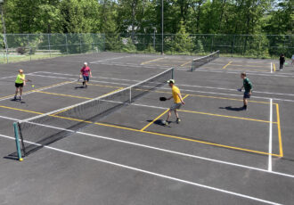 People play pickleball lined on tennis courts.